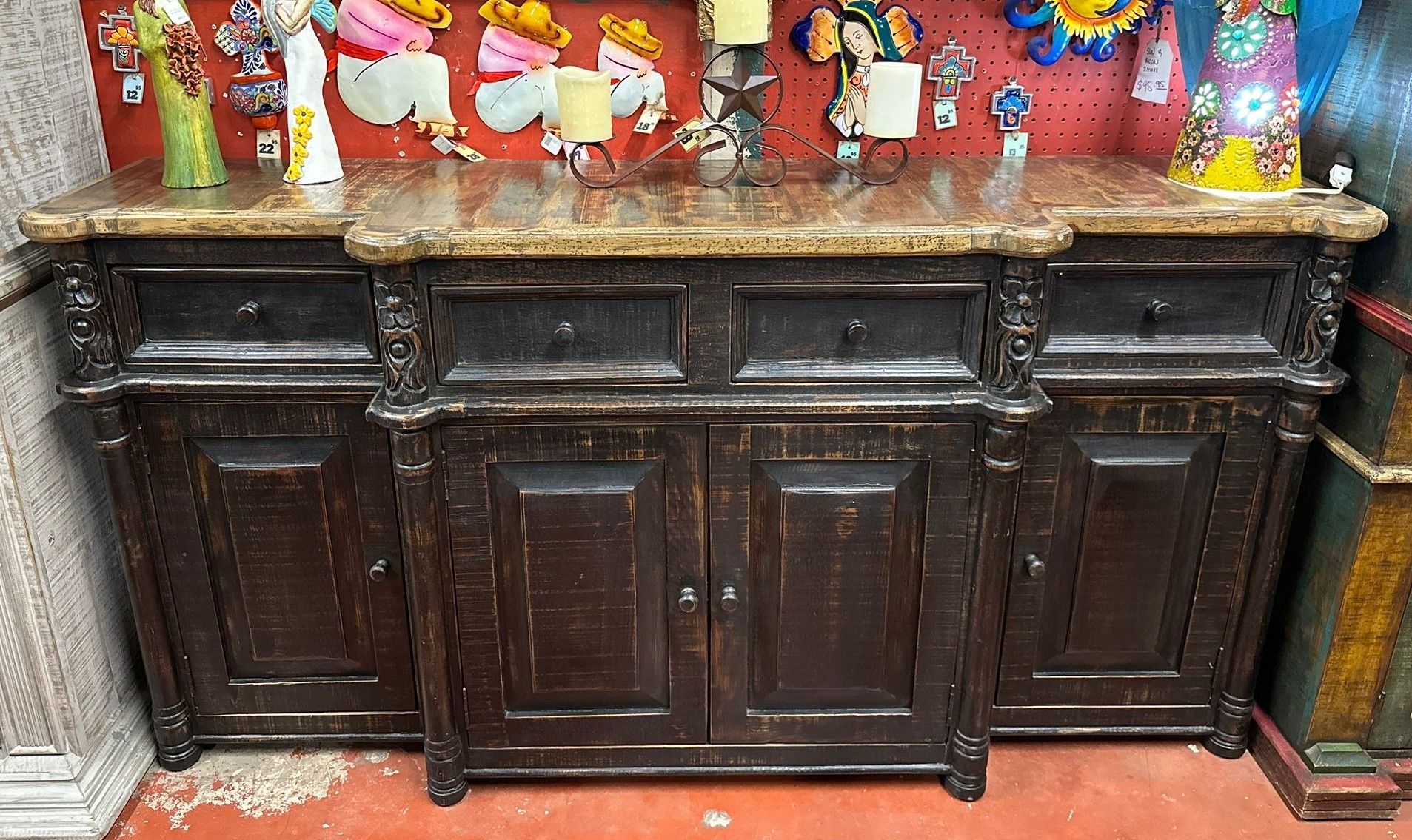 Dark wooden buffet with marble top and ornate carvings; displayed in a shop with colorful decorations in the background.