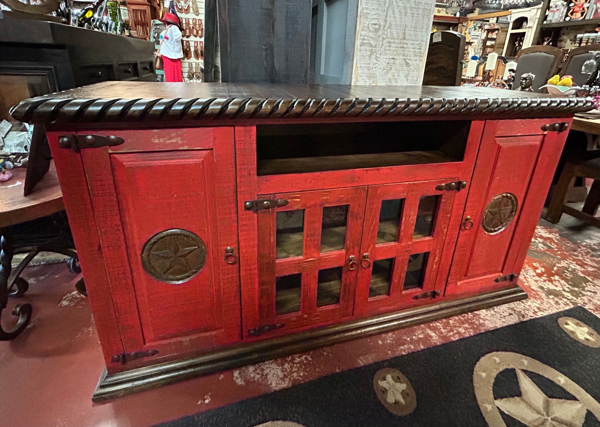 Red and brown wooden media console with glass-fronted doors and decorative hardware, set in a store.