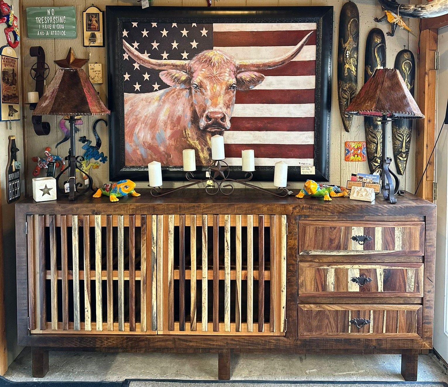 Rustic wooden cabinet with a framed longhorn over an American flag, flanked by lamps and candles.