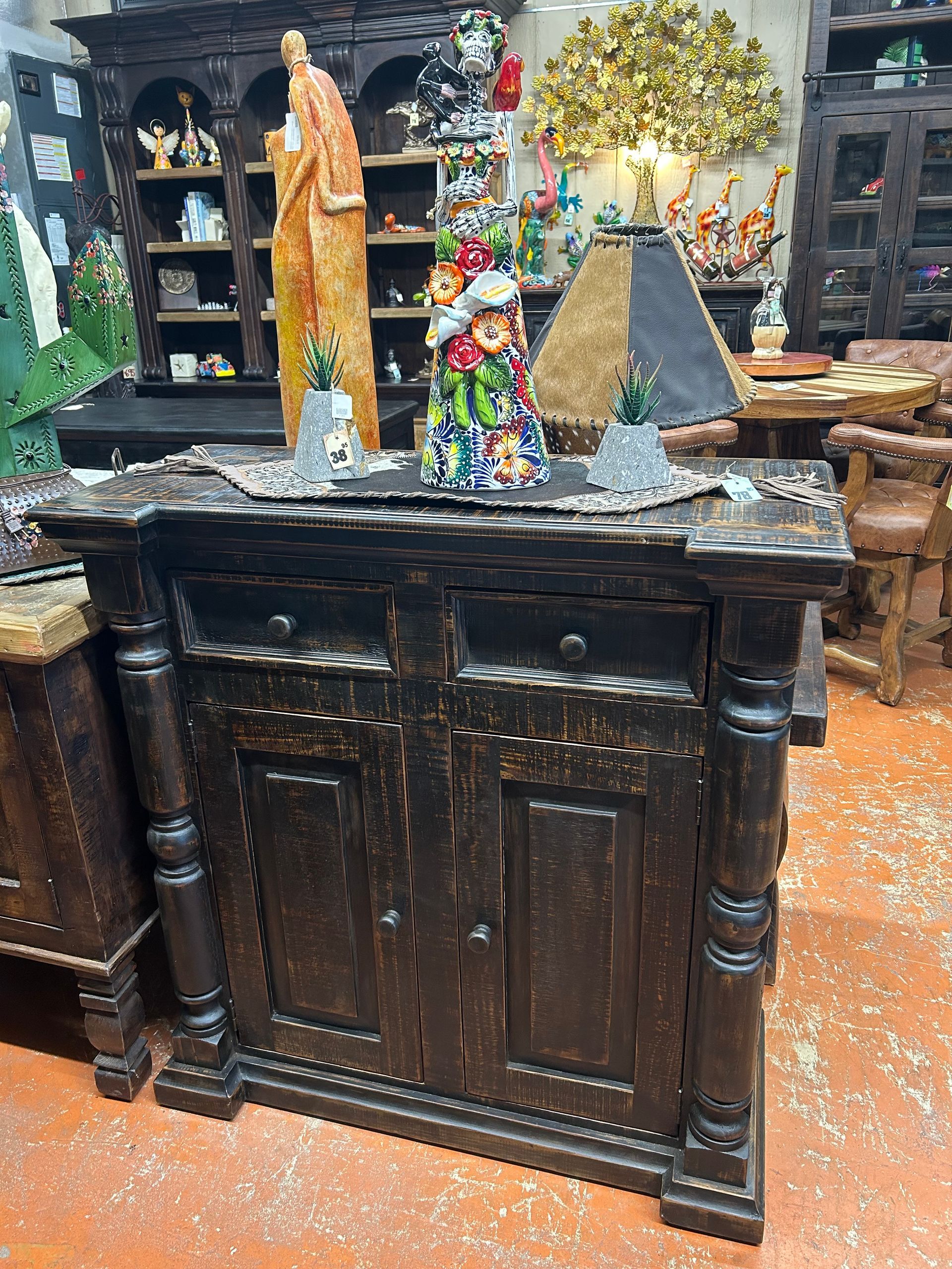 A distressed black wooden cabinet with two doors and two drawers, decorated with small plants and a figurine.