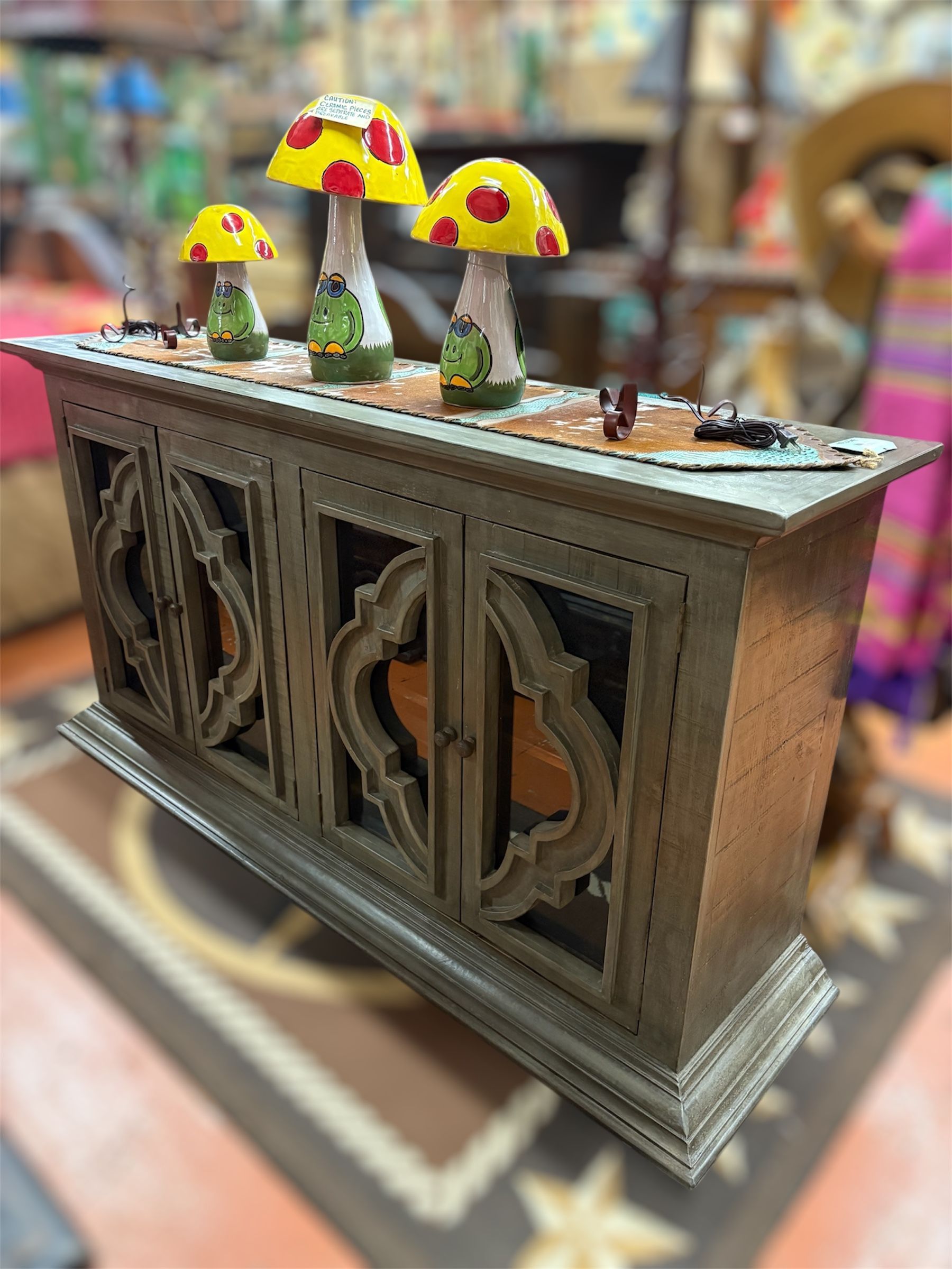 A wooden cabinet with carved doors holds colorful mushroom decorations. The setting appears to be a shop or showroom.