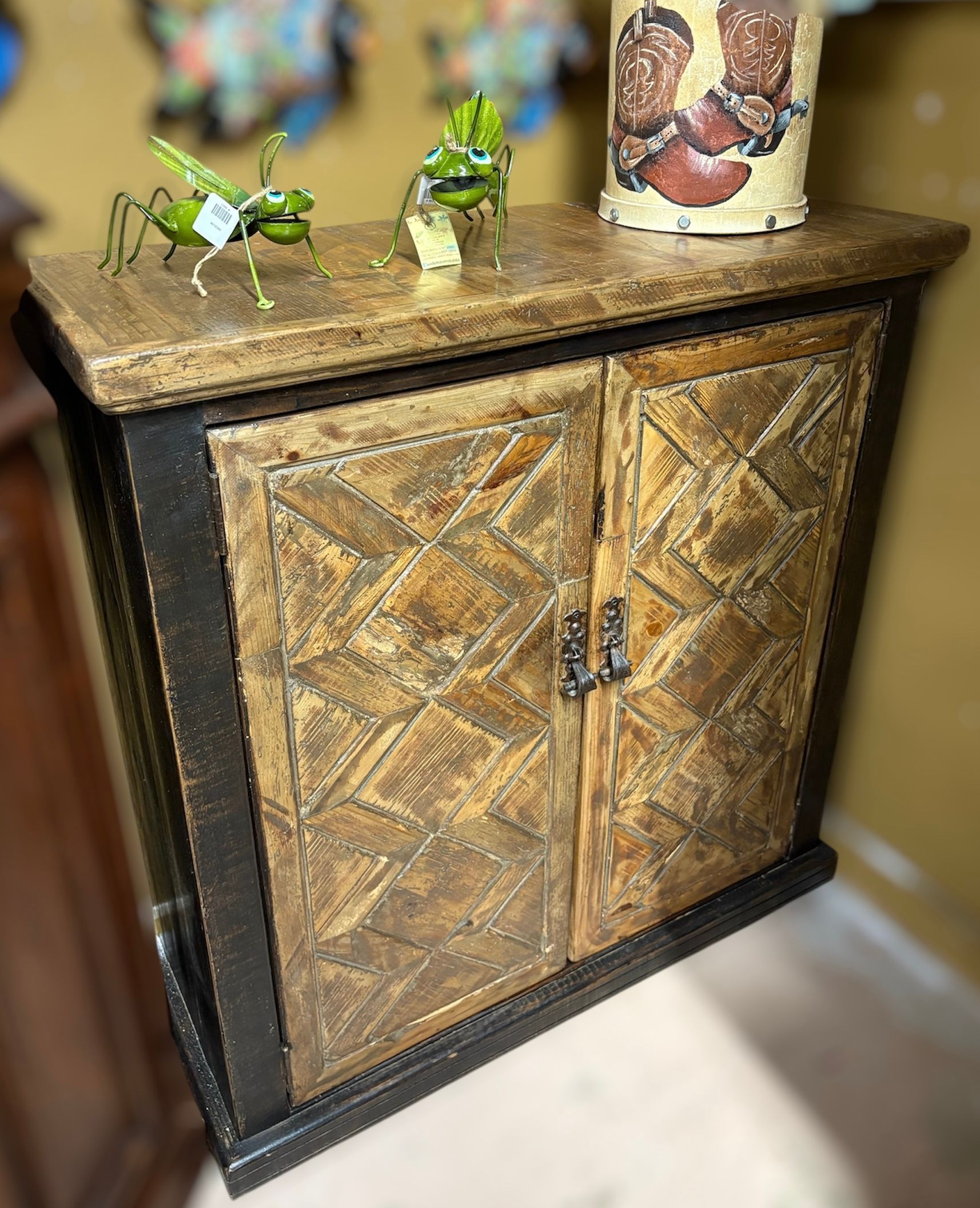 A rustic wooden cabinet with textured doors and a decorative top, holding small figurines.
