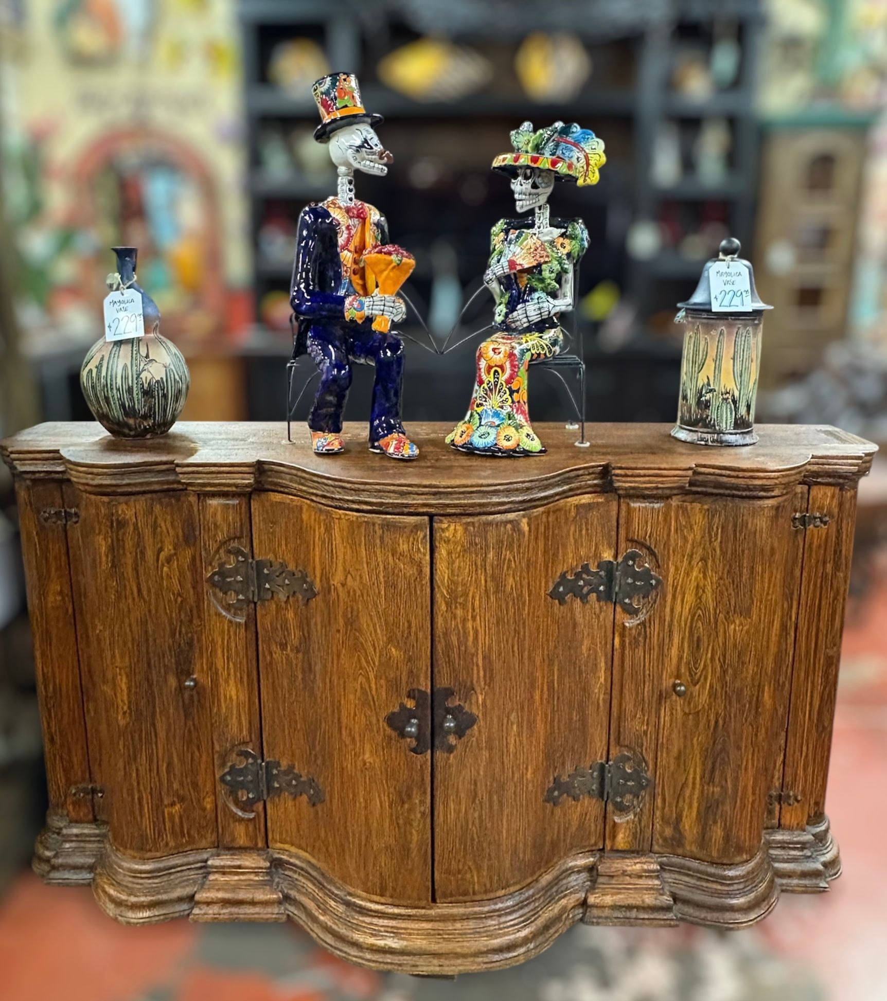 A wooden cabinet with skeletal figures on top, set against a colorful background. The skeletons are dressed in vibrant clothing.