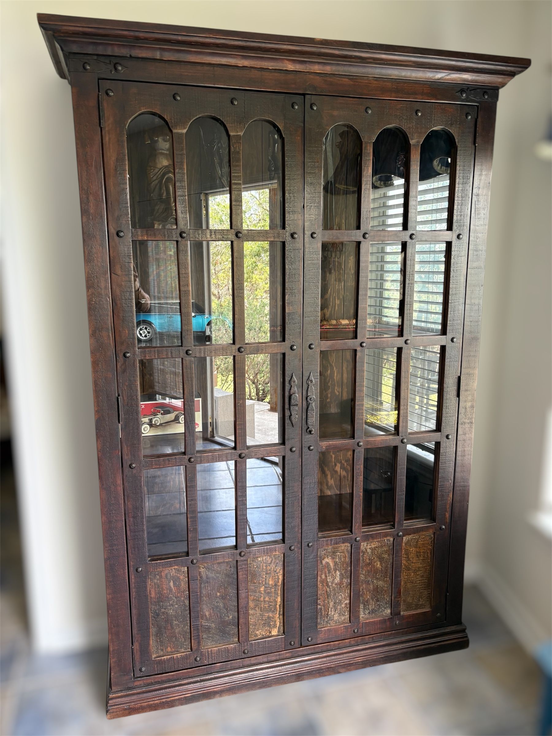 Dark wooden cabinet with glass doors and a decorative top, likely used to display items. The cabinet appears to be indoors.