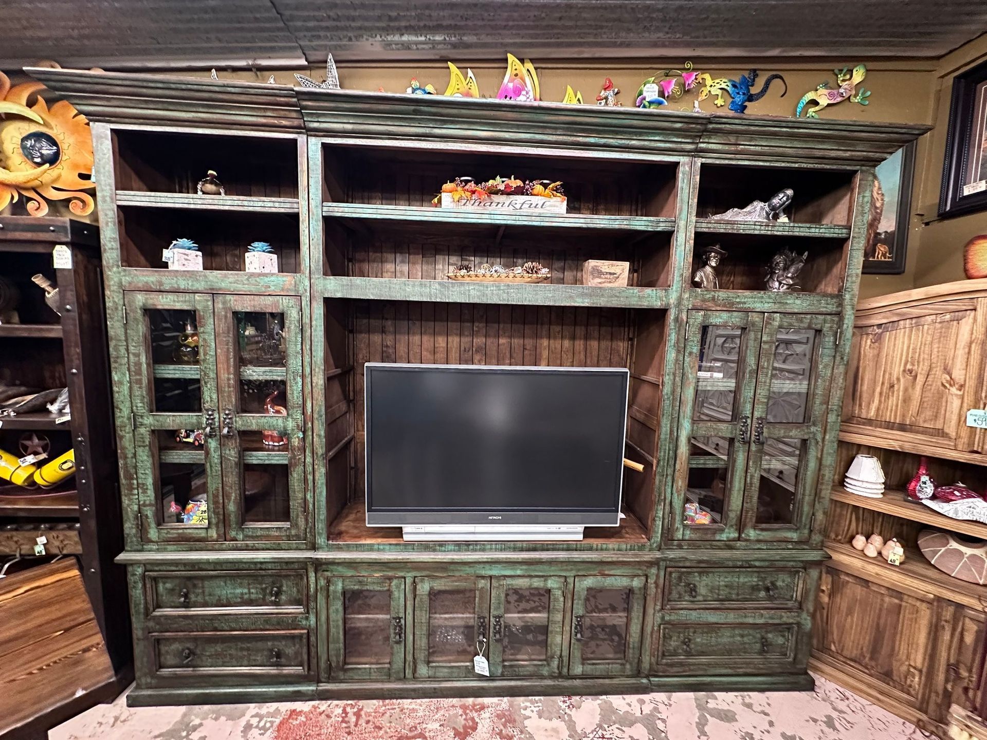 Large, weathered green wooden entertainment center with a TV and glass-doored cabinets filled with decor.