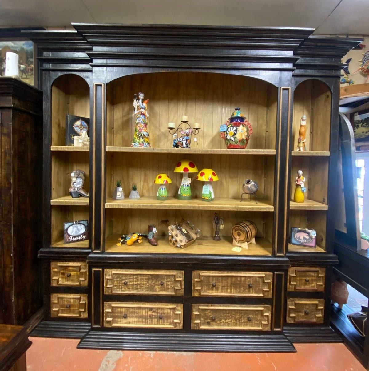 Dark wood cabinet with shelves and drawers displaying various decorative items against a light wood backdrop.