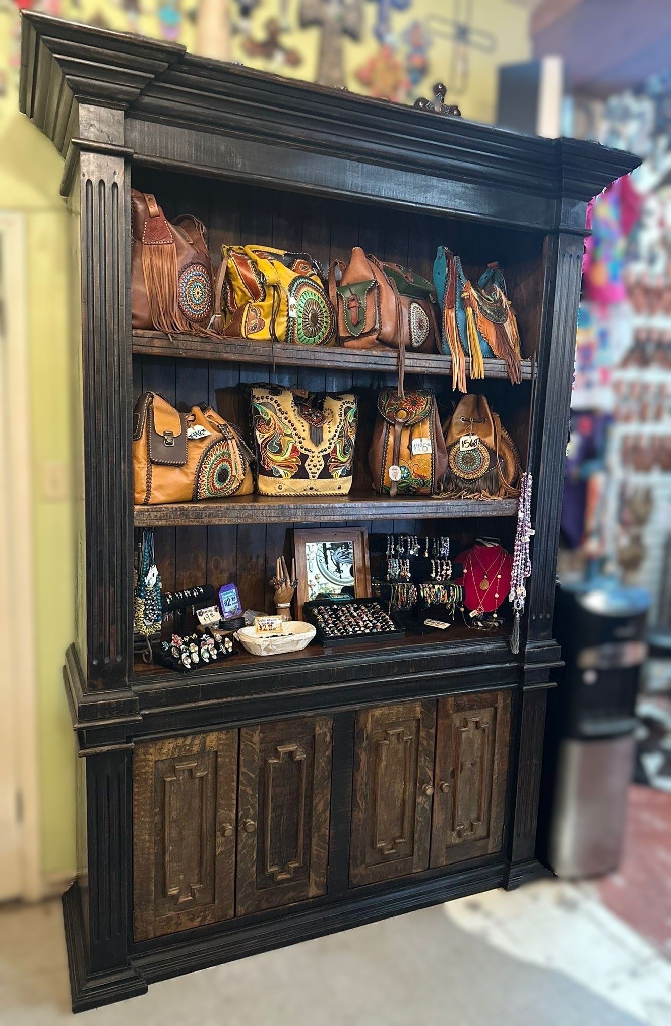 Black wooden cabinet displaying various colorful artisan bags and accessories.