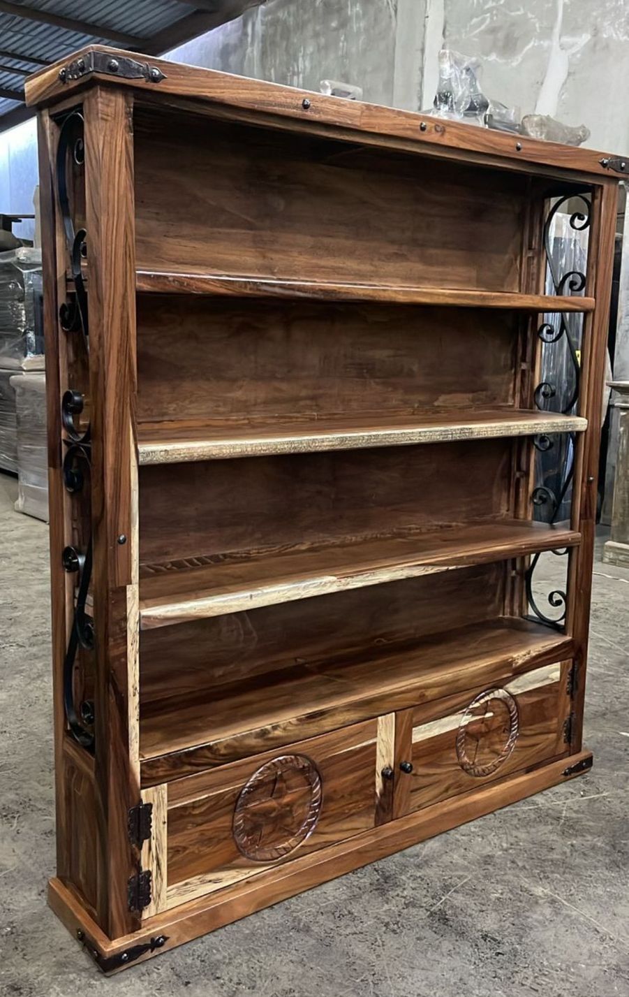 Wooden bookshelf with ornate metalwork and two bottom doors, filled with shelves of varying heights.