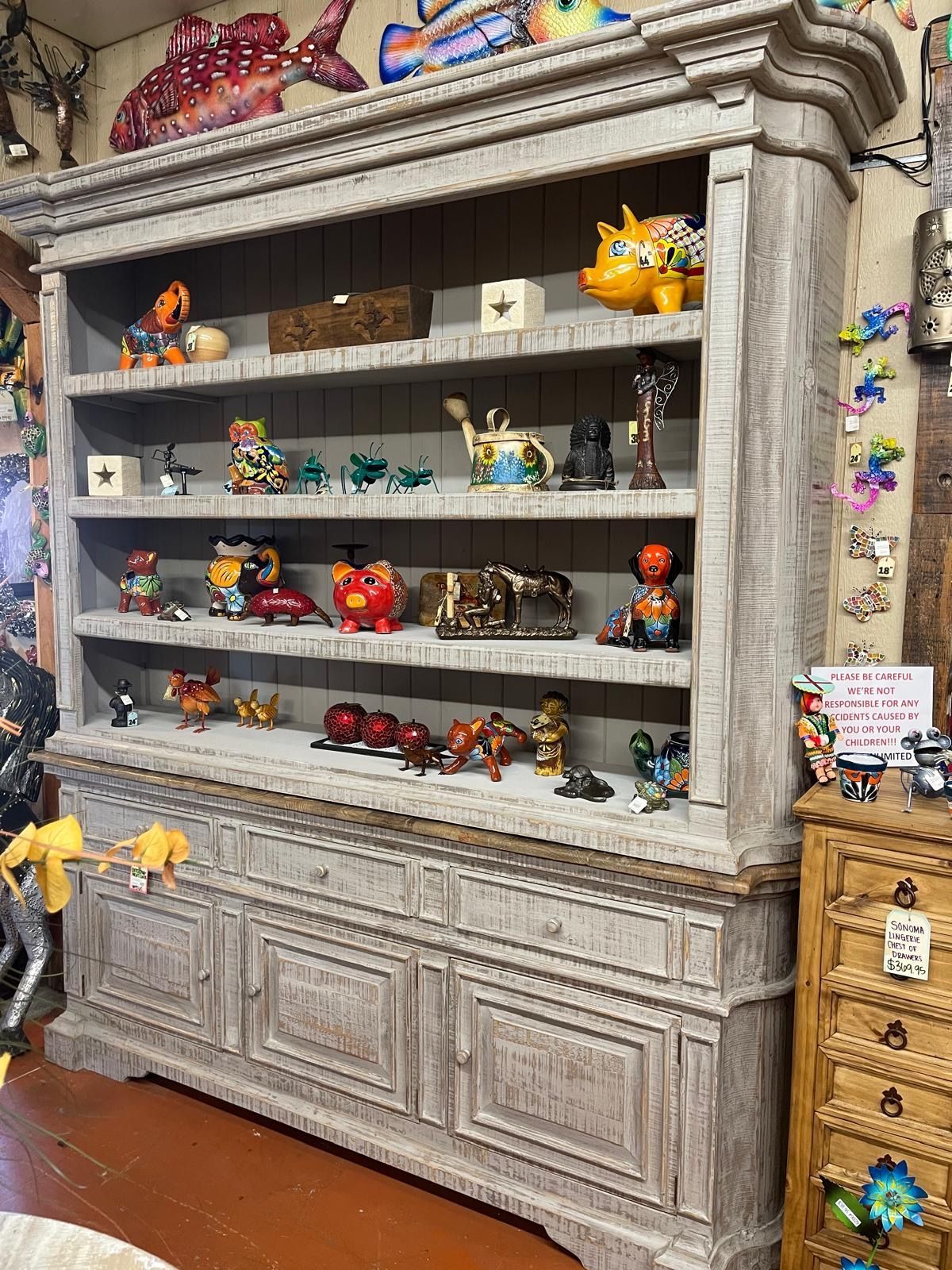 Large gray-washed cabinet filled with colorful figurines and decorative items, displayed in a shop setting.