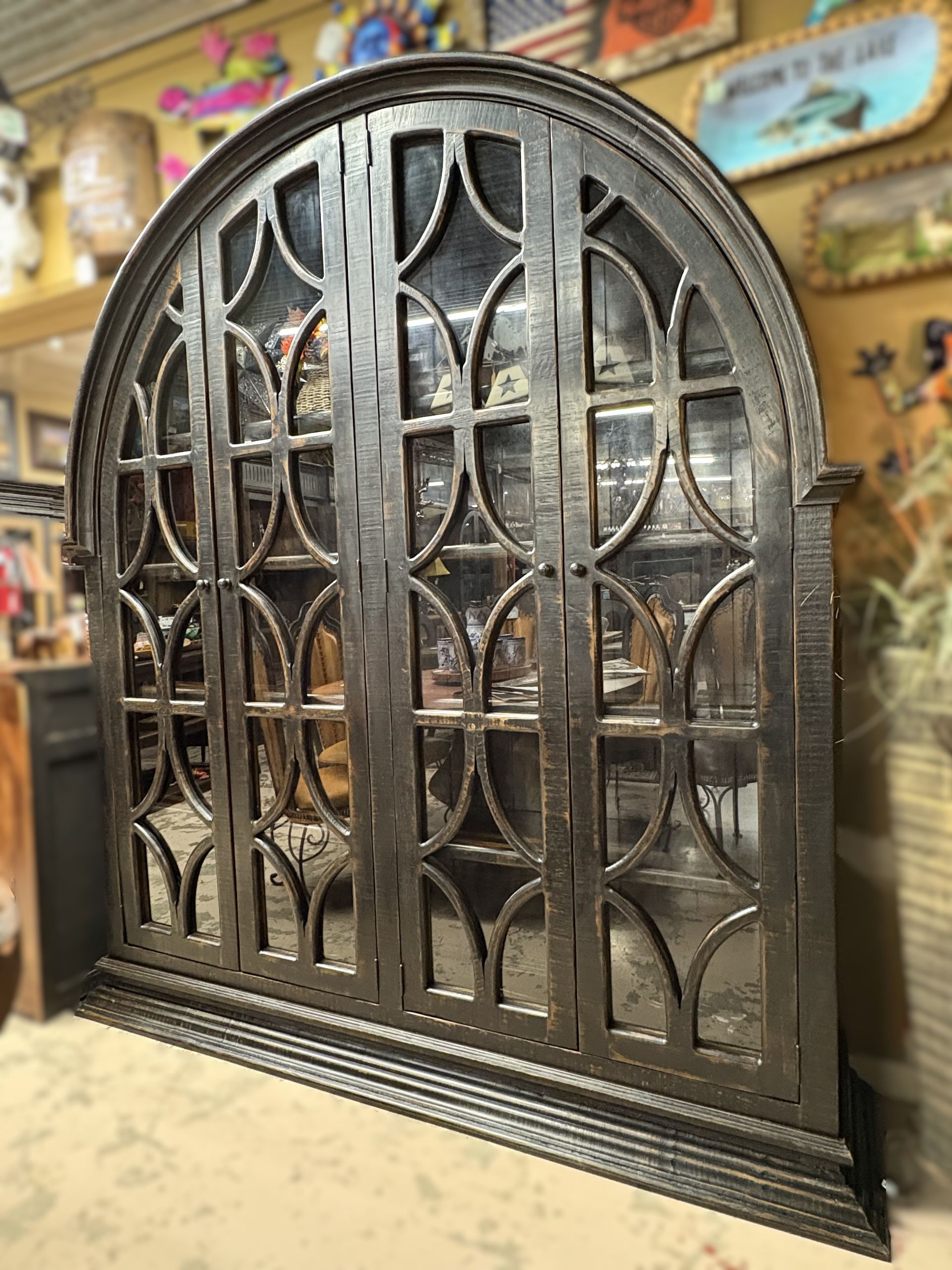 Black metal cabinet with arched top and multiple glass-paned doors. It has ornate circular and vertical detailing.