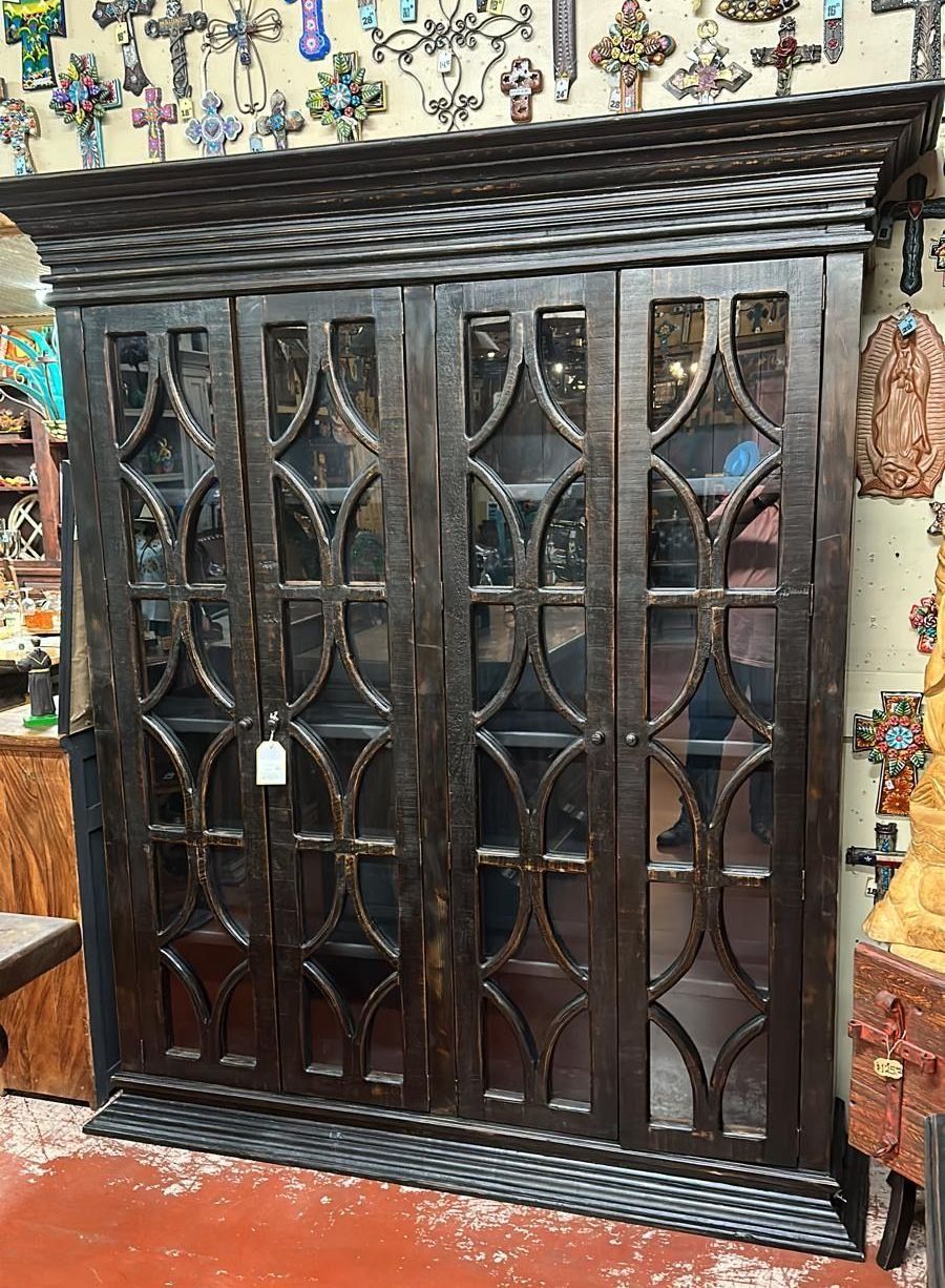 Large, dark wood cabinet with glass doors featuring decorative, geometric patterns. It is in a room with religious artifacts on the walls.