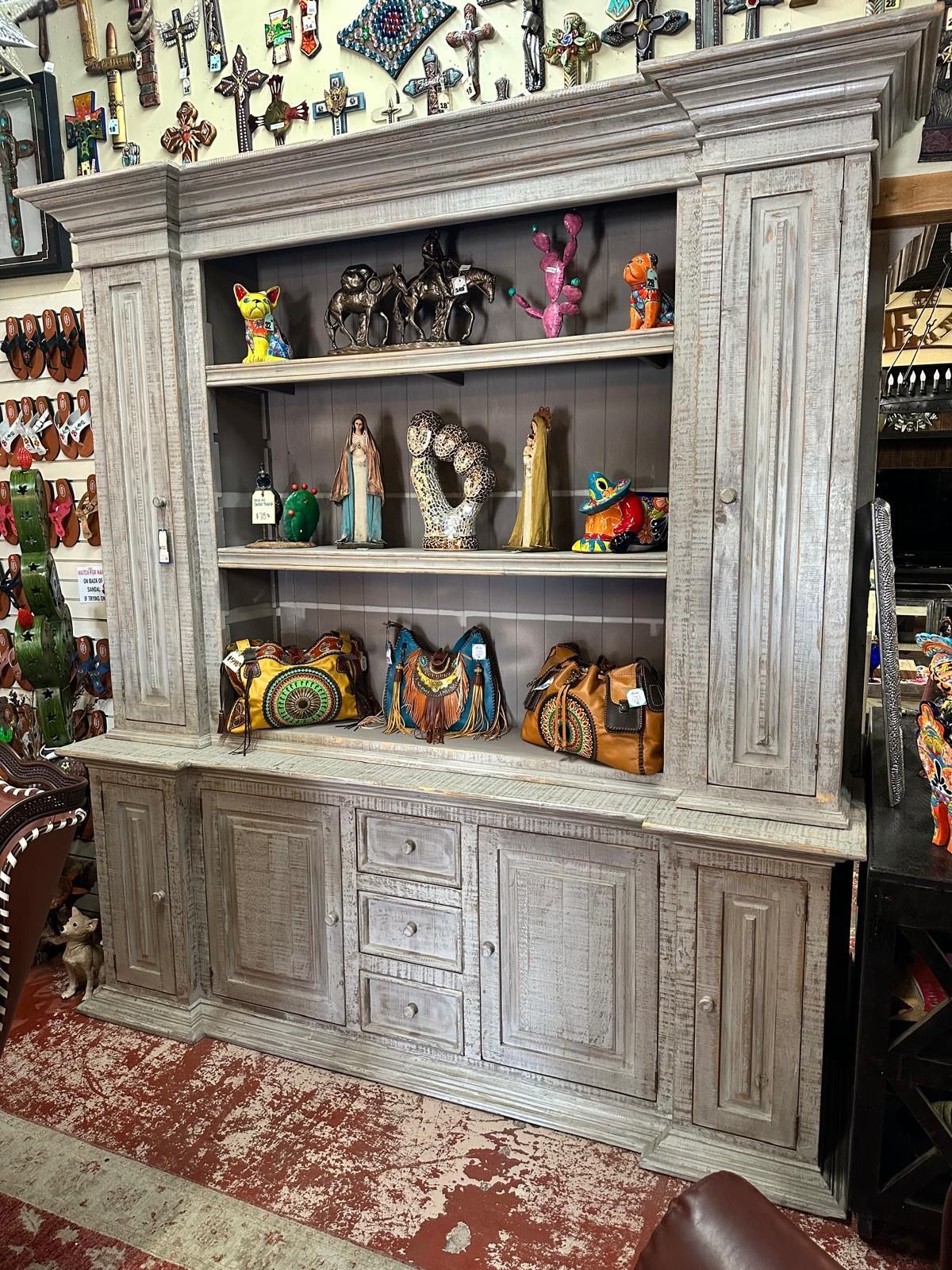 A rustic, gray wooden hutch displays pottery and handbags on shelves, with a red-speckled floor.