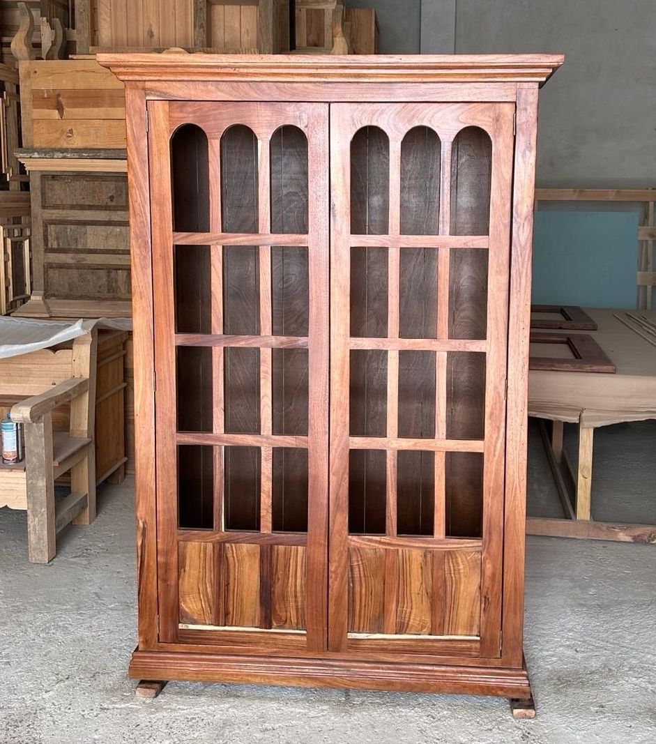 Wooden cabinet with two glass doors and arched windowpanes, likely in a woodworking workshop.