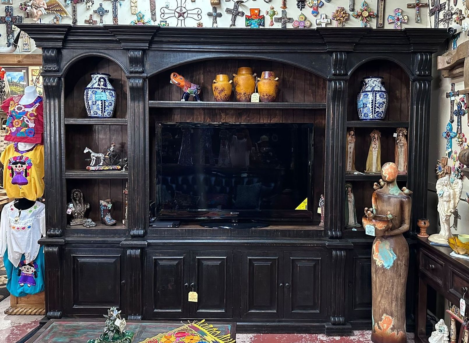 Large black entertainment center with shelves, holding vases and statues, a television in the center.