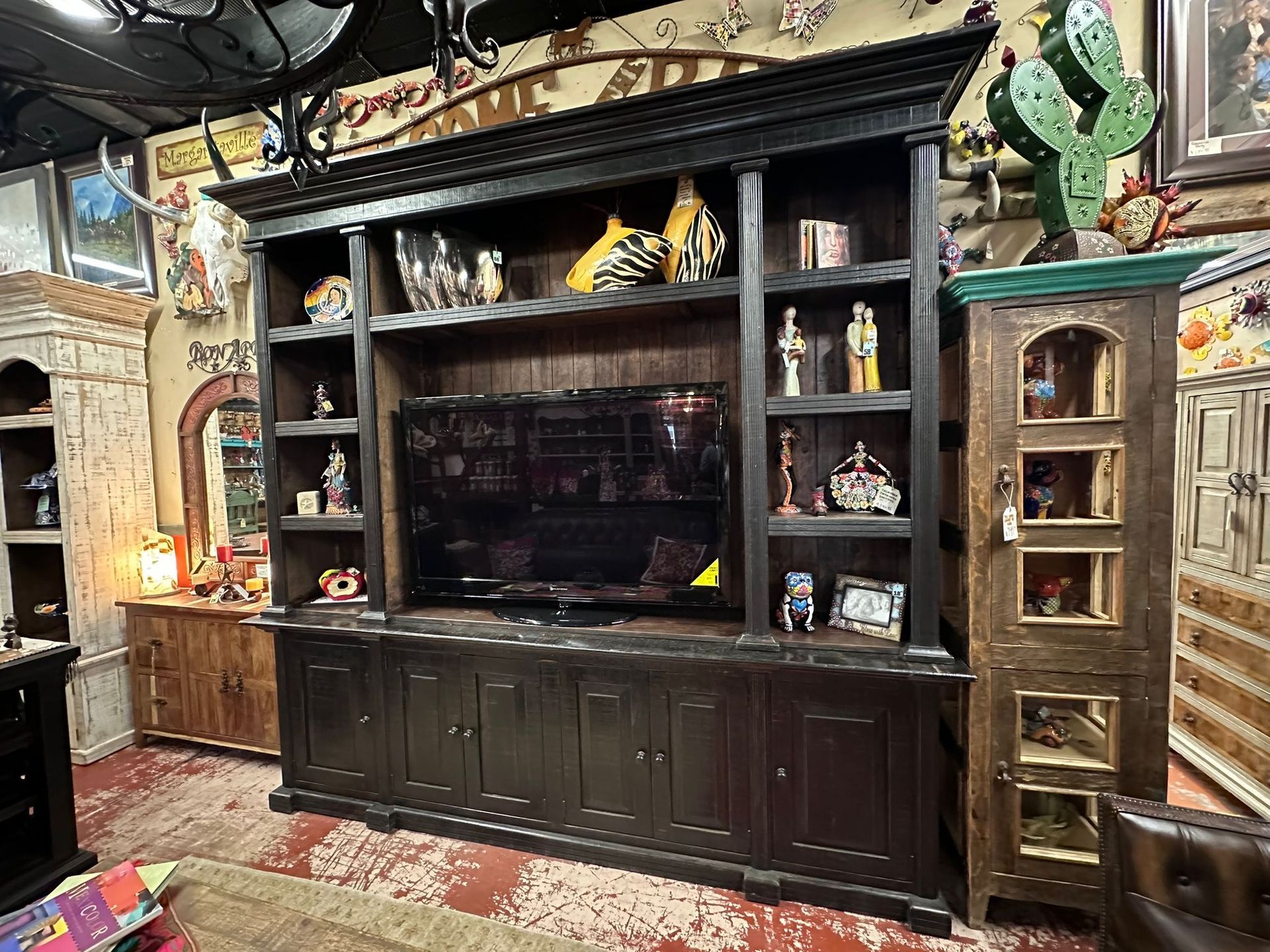 Black wooden entertainment center with TV and shelves, filled with decorative items, in a cluttered room with rustic decor.
