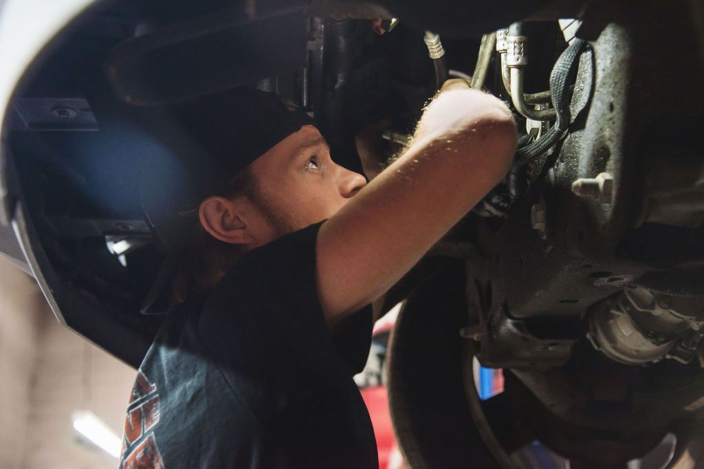 Mechanic inspecting the underside of a vehicle with a flashlight in a garage
