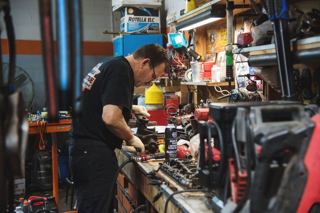 Mechanic working on a car engine in a cluttered auto repair shop, surrounded by tools and equipment