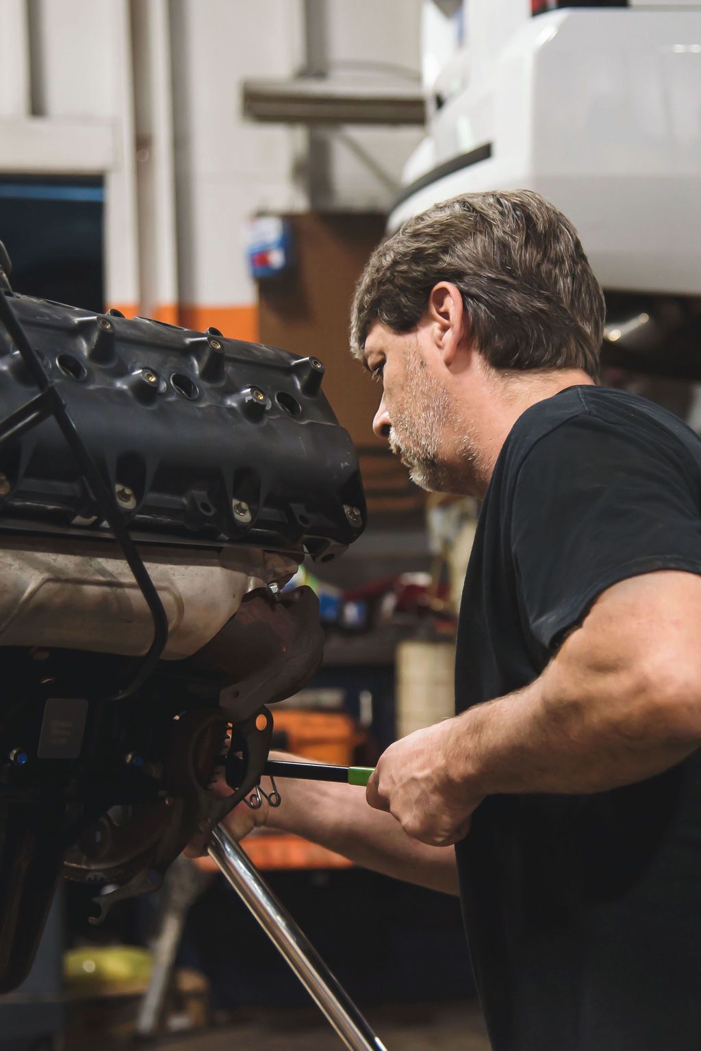 Mechanic working on a car engine in a garage, leaning over the open hood.