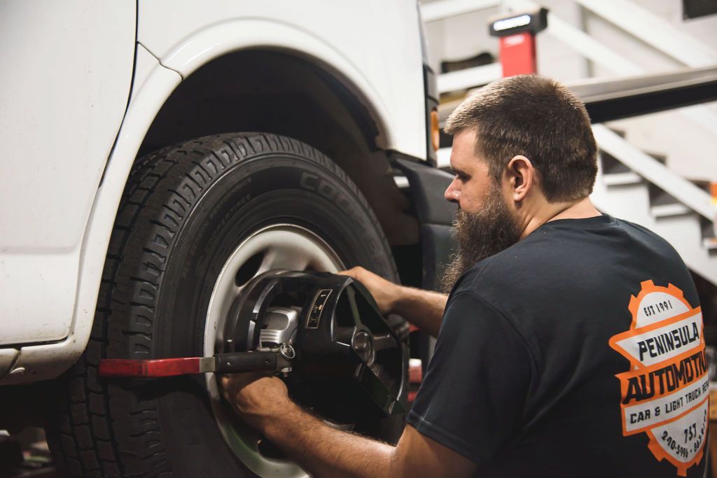 Mechanic working on a white vehicle’s wheel with a tire balancing machine in an auto shop