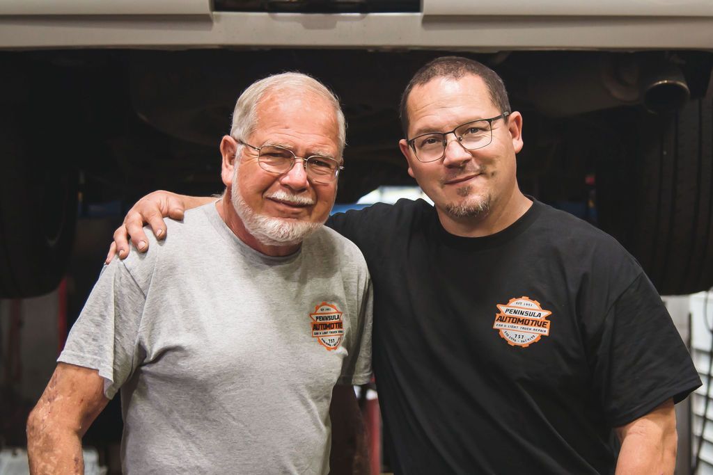 Two people standing side by side and smiling in black and gray T-shirts with arms around each other.