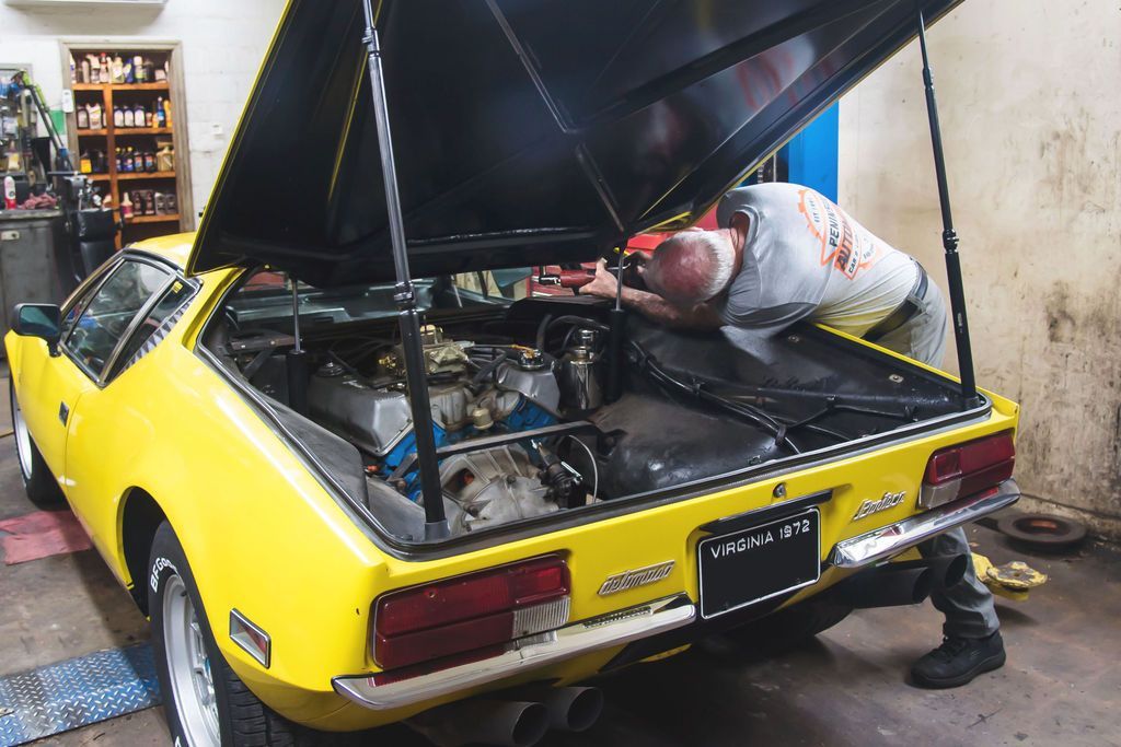 Mechanic working under the open hood of a yellow sports car in a garage