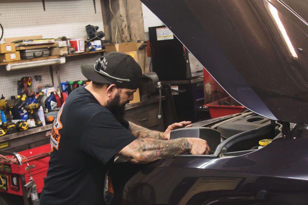 Mechanic working under a car hood in a workshop, with tools and shelves in the background