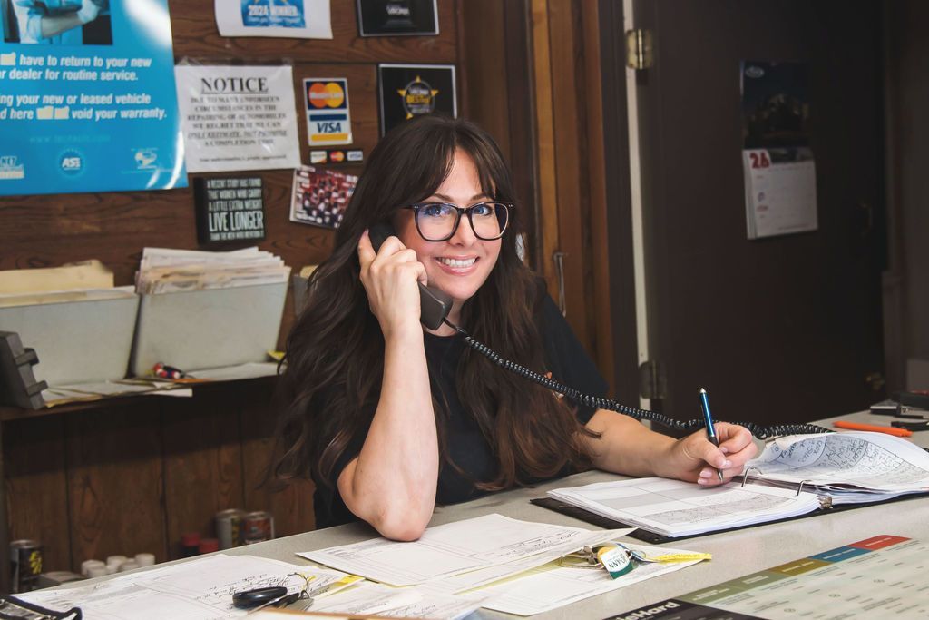 Woman at a desk in an office, smiling and talking on a phone while writing in a notebook.