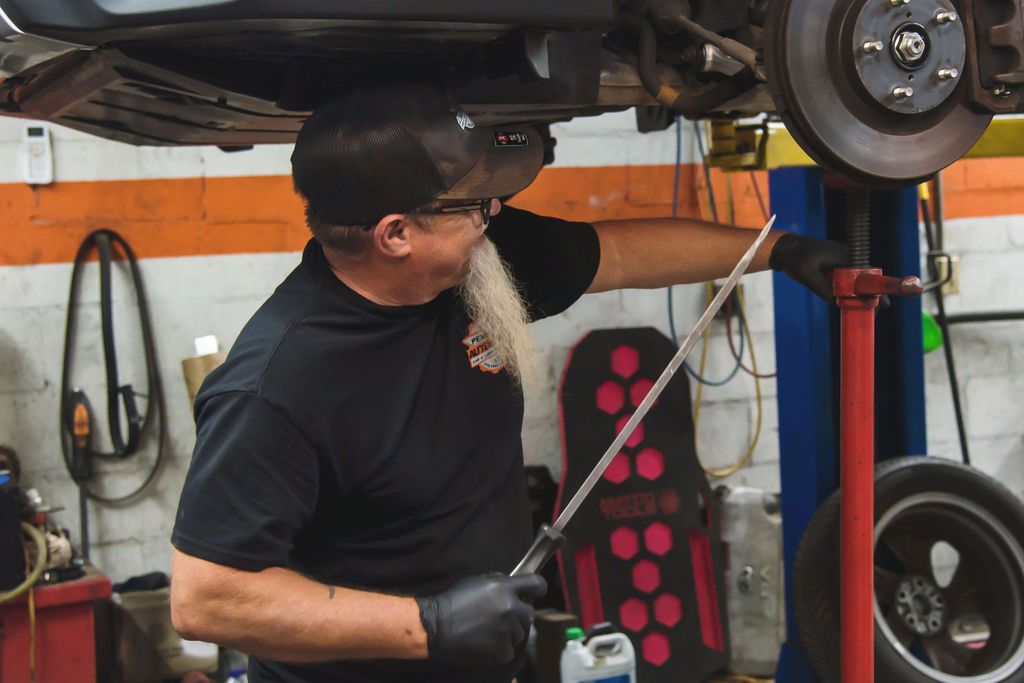Mechanic inspecting a car on a lift in an auto shop, reaching up toward the undercarriage.