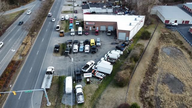 Aerial view of a busy truck yard beside a road, with many parked vehicles and a warehouse.