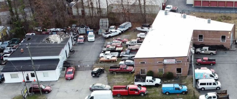 Aerial view of a crowded parking lot beside brick buildings with many cars and trucks.