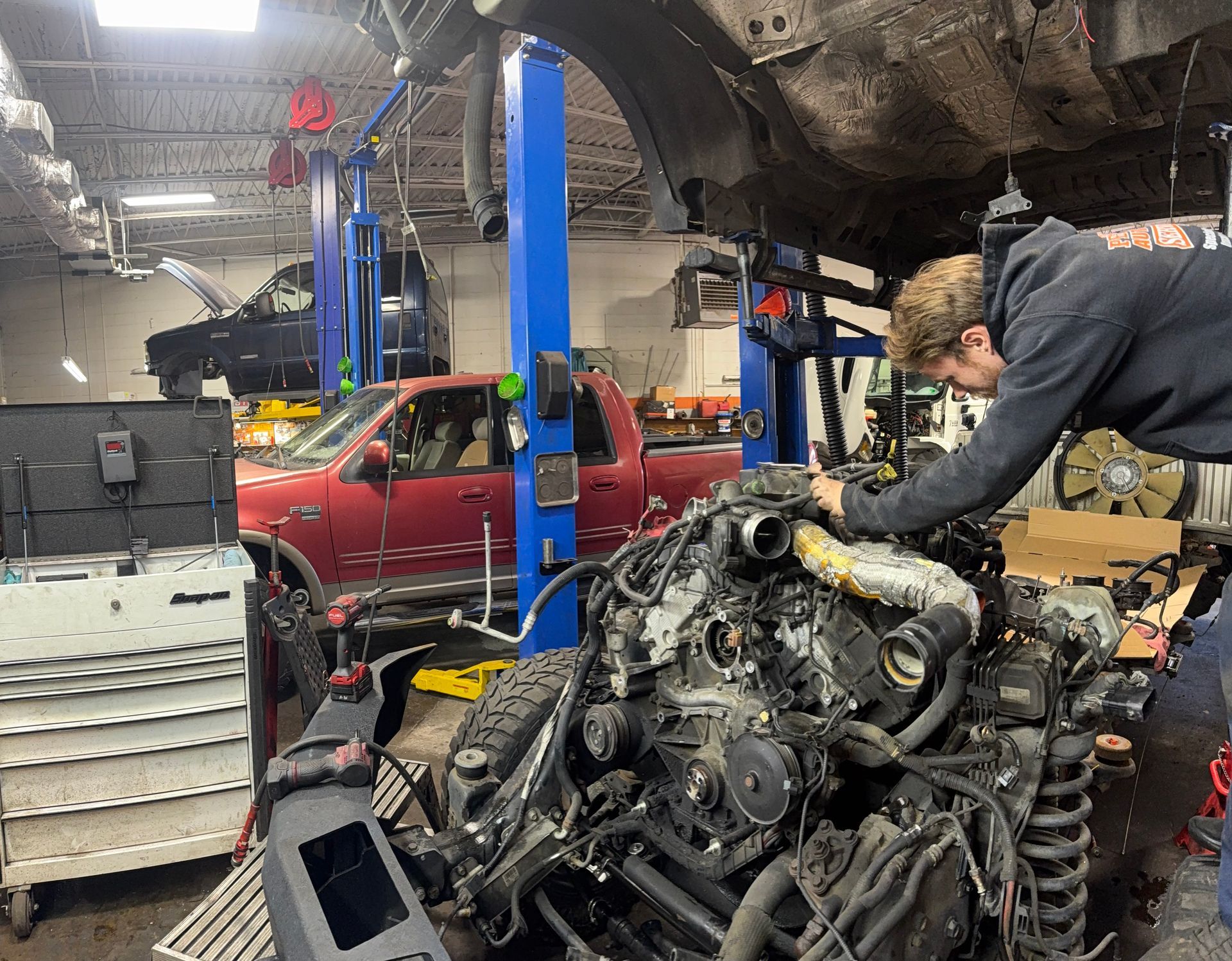 Mechanic working on a car engine in an auto repair shop under a lifted vehicle