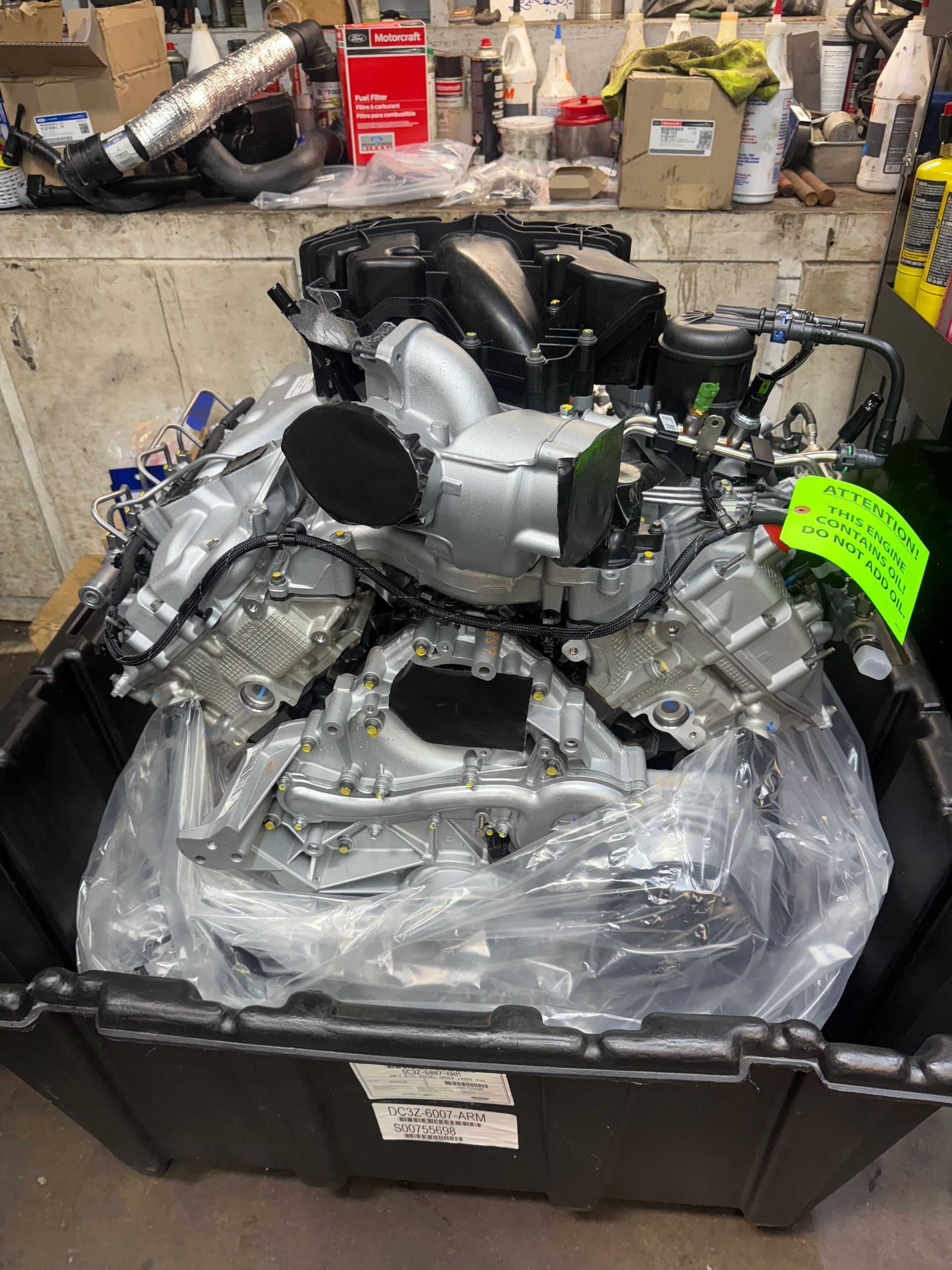 Large black plastic container filled with wrapped machinery parts in a workshop, with a neon green tag attached