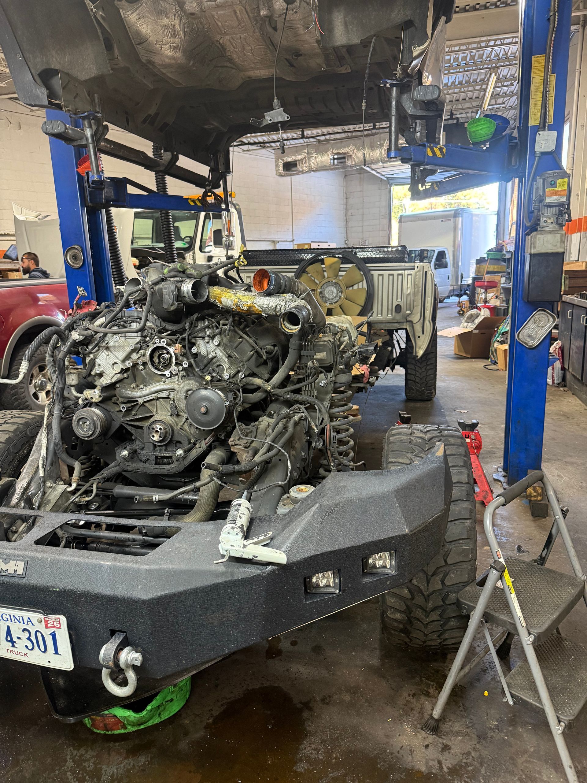 Auto repair shop with a car lifted on a blue hoist and a disassembled engine on a trailer below.