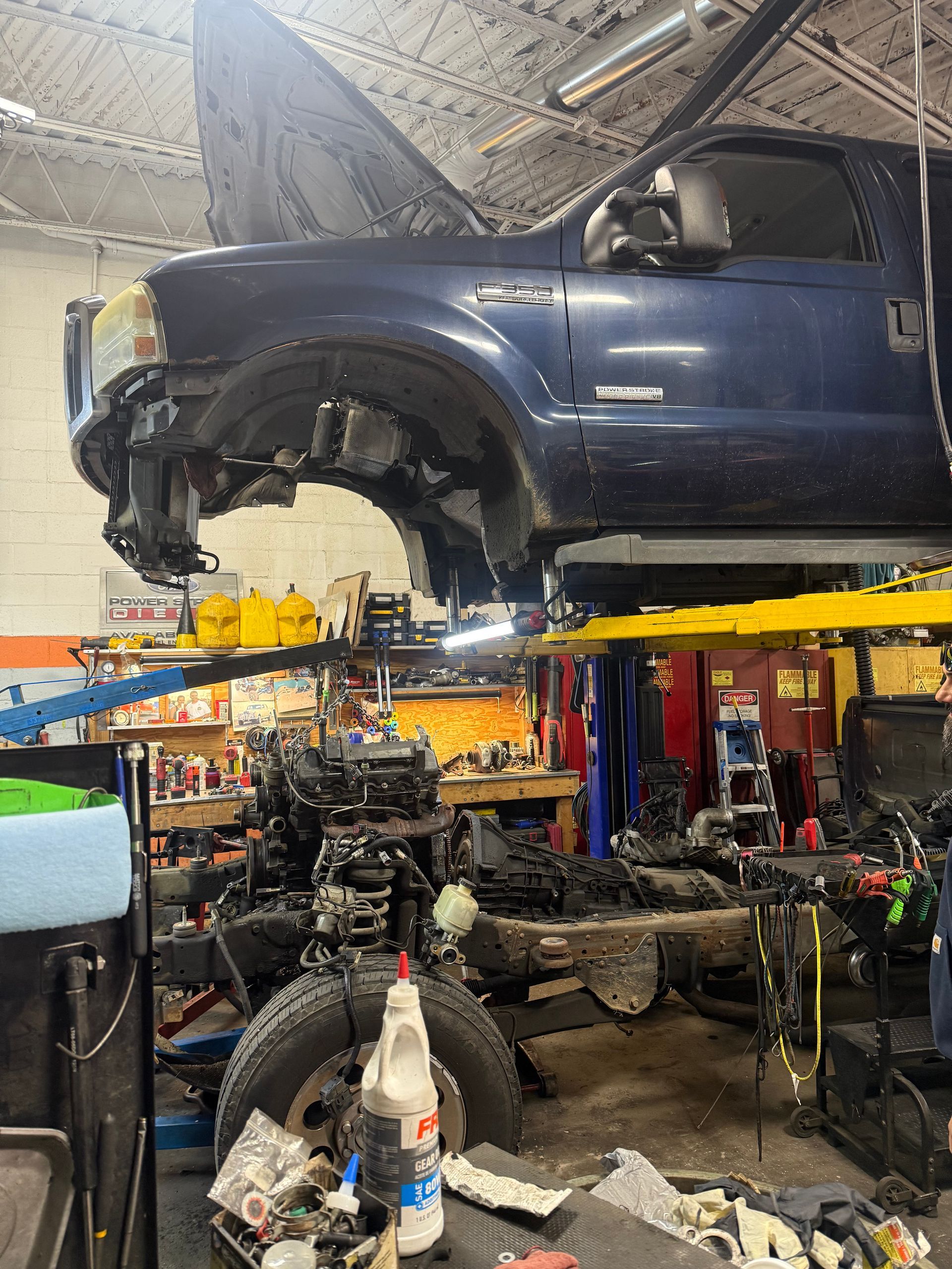 Blue pickup truck lifted on a shop hoist inside an auto repair garage with engine parts below