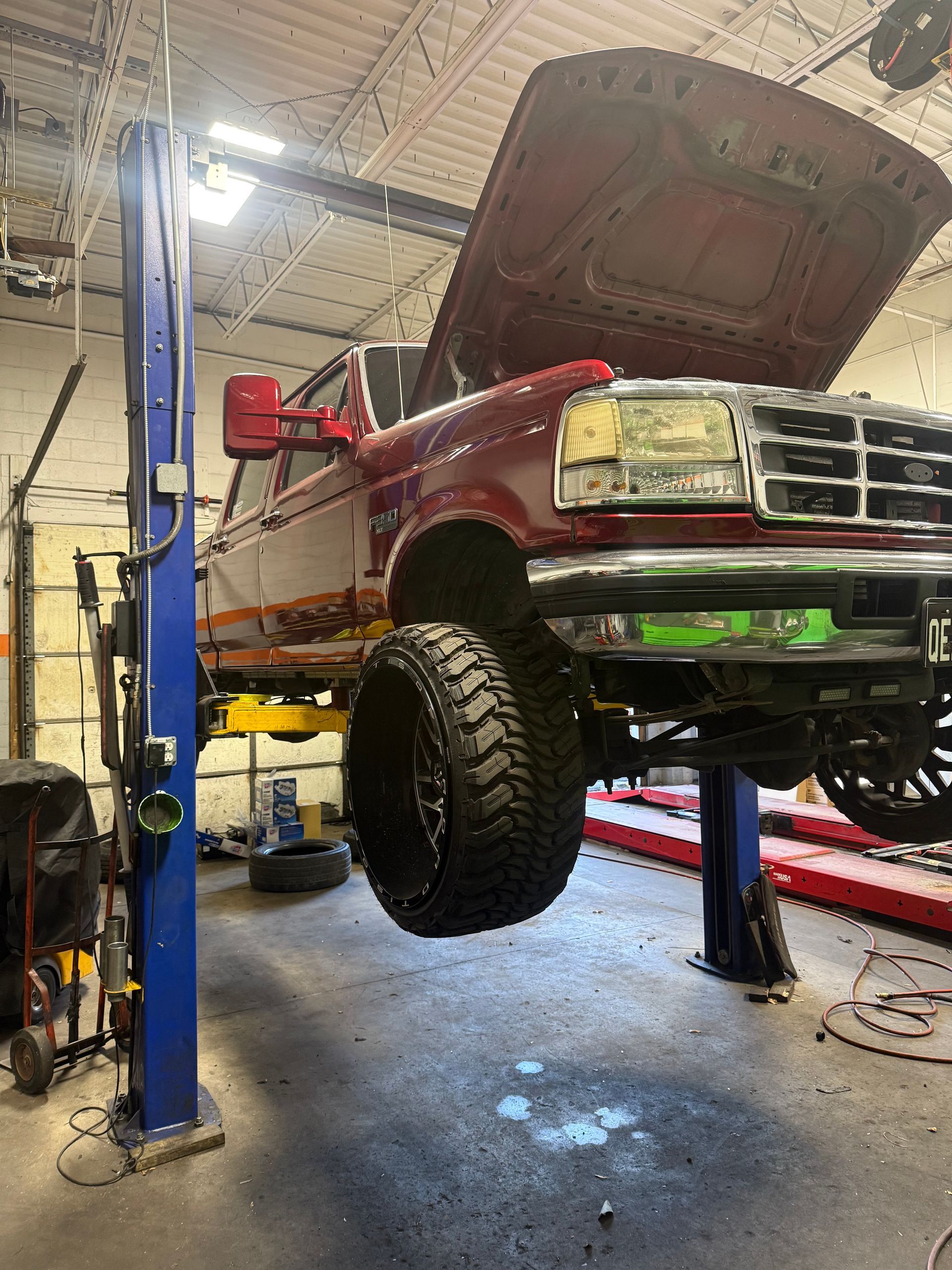 Red pickup truck lifted on a shop hoist with hood open in a garage