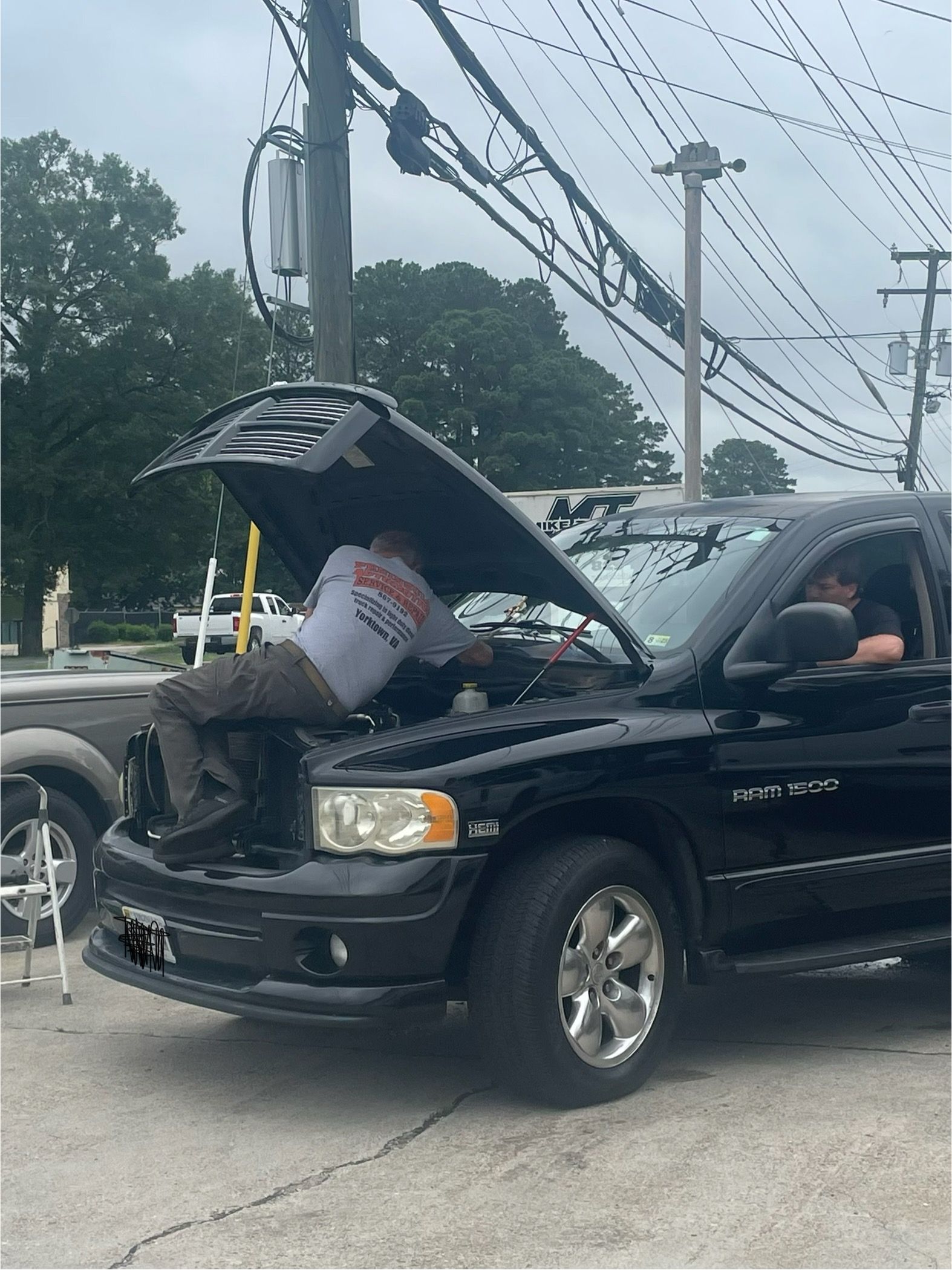 Black SUV with hood open after a crash, damaged front end, bucket in engine bay, utility poles in background