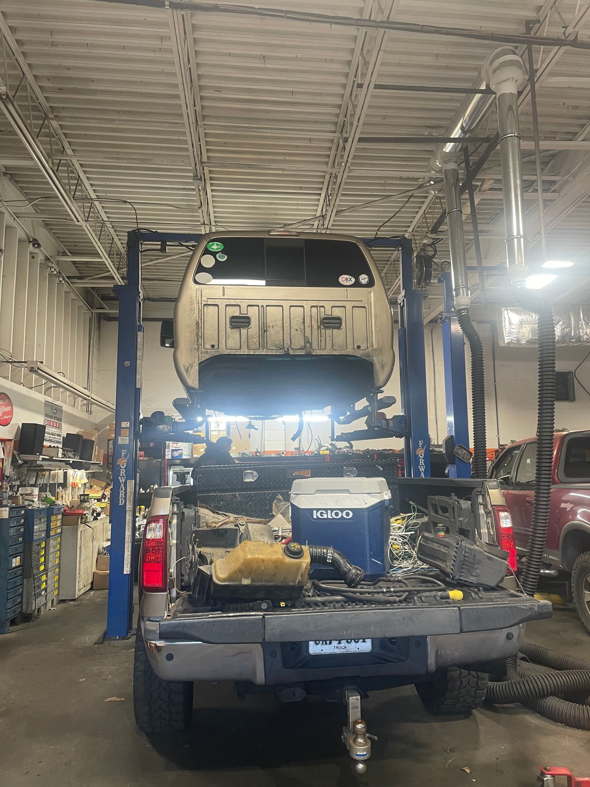 Blue vehicle on a lift in an auto repair garage with the front bumper removed