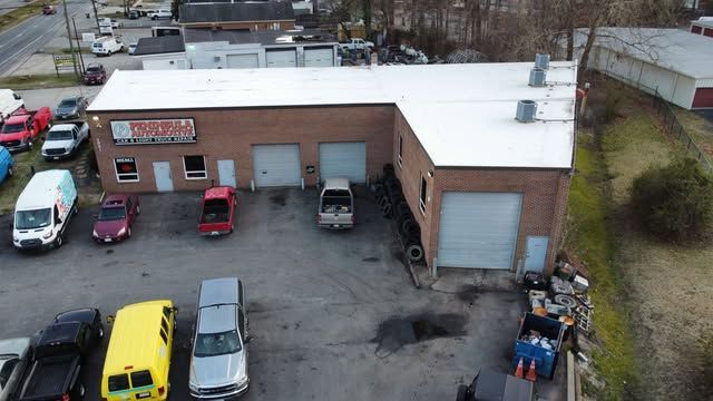 Aerial view of a brick auto repair shop with parked cars in the lot and snow on the roof