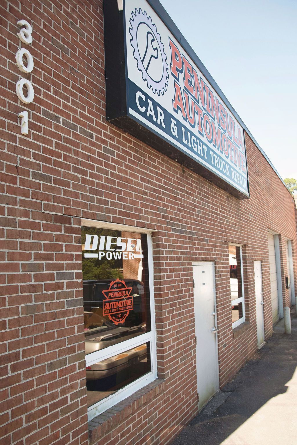 Brick storefront with car audio shop sign and windows along a sidewalk, street number 3001 on the wall