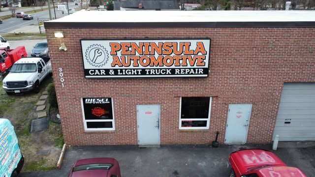Peninsula Automotive storefront with brick facade, orange sign, and parked vehicles outside