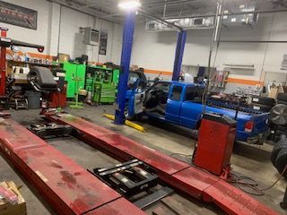 Auto repair shop with a blue pickup on a lift, red frame rails, and green equipment in the background