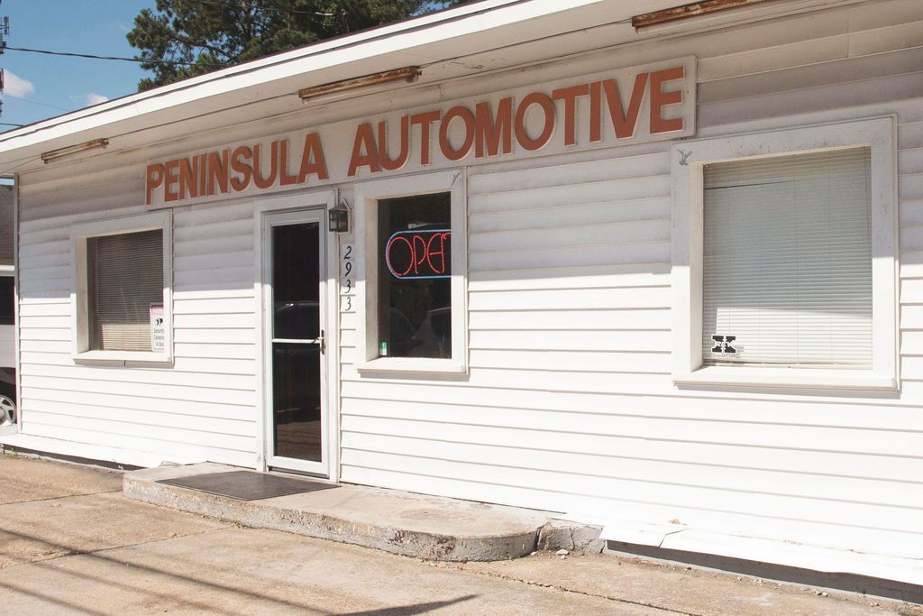 Small white storefront with “PENINSULA AUTOMOTIVE” sign and open door, viewed from the sidewalk.