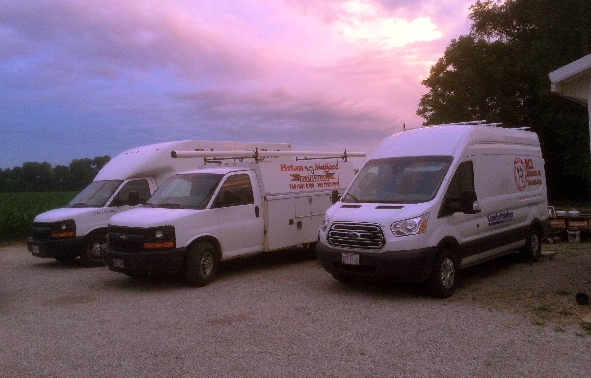 Three white vans are parked in a gravel lot