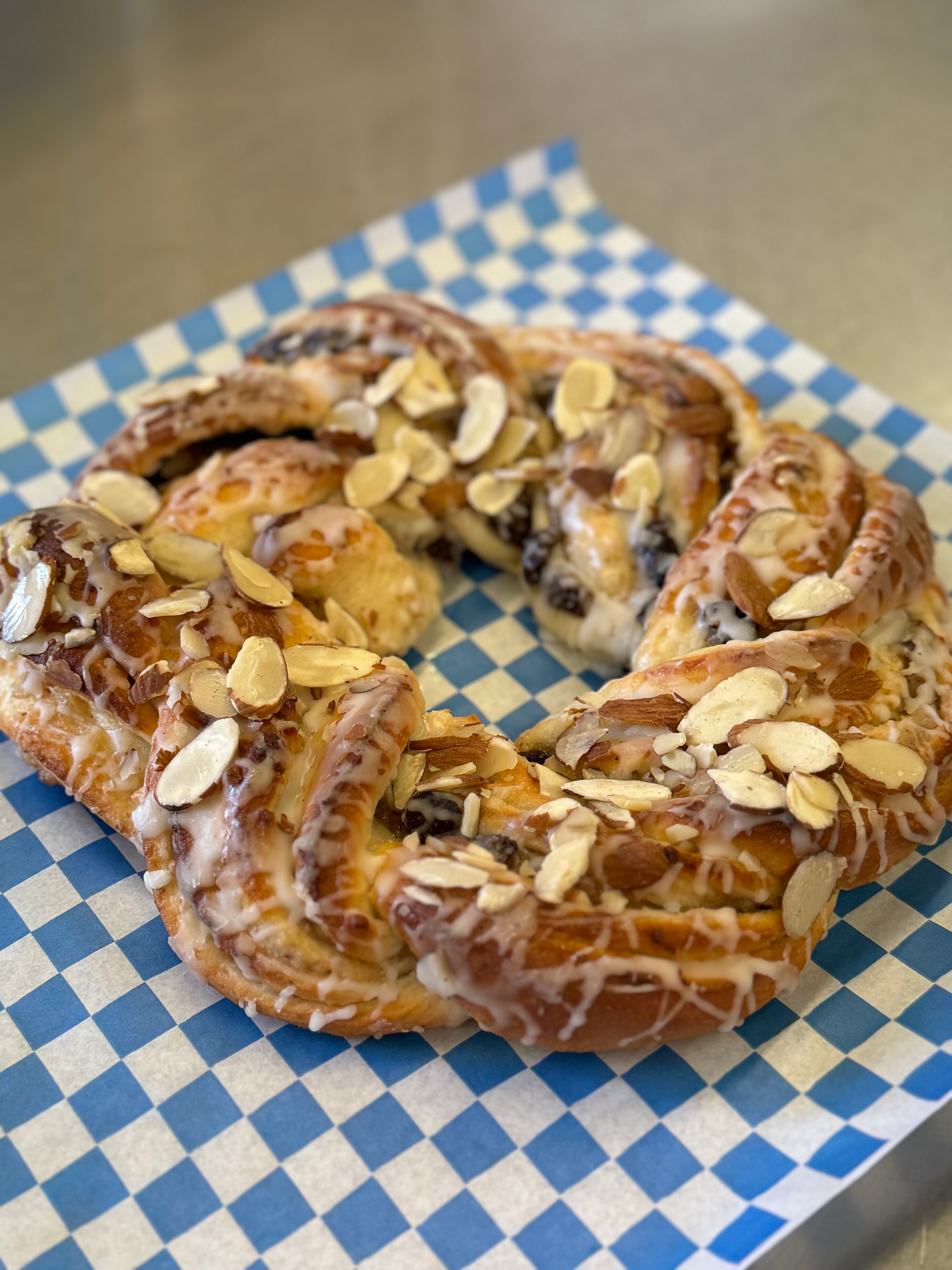 Almond-topped glazed pastry ring on blue-and-white checkered paper tray liner