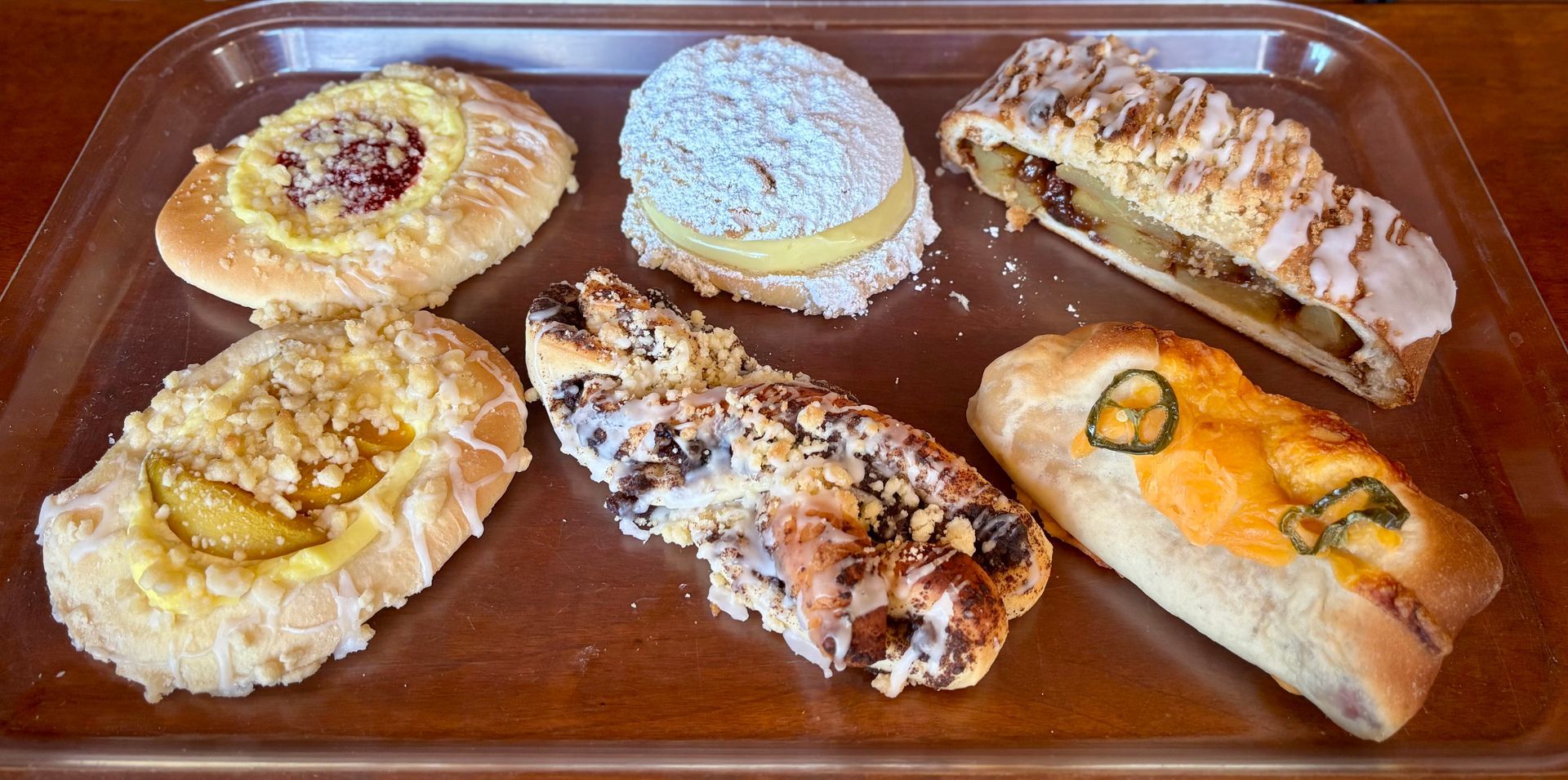 Assorted decorated pastries and pastries on a tray, including iced donuts and a frosted pastry with fruit