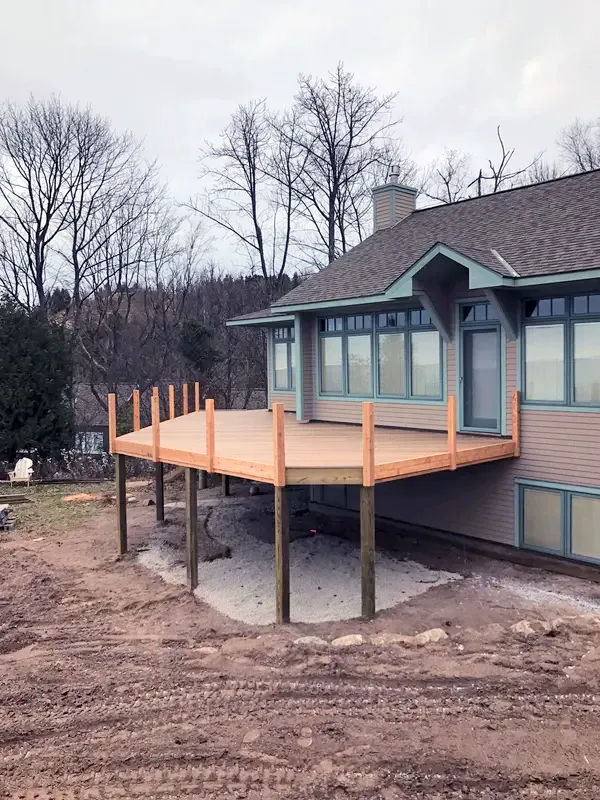 Raised wooden deck under construction beside a house in a wooded yard