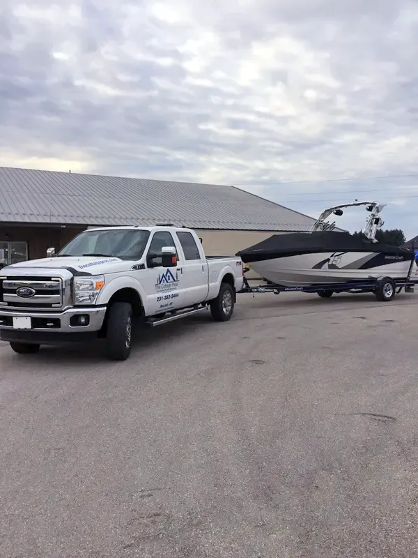 White pickup towing a black-and-white speedboat on a trailer in a parking lot under cloudy skies