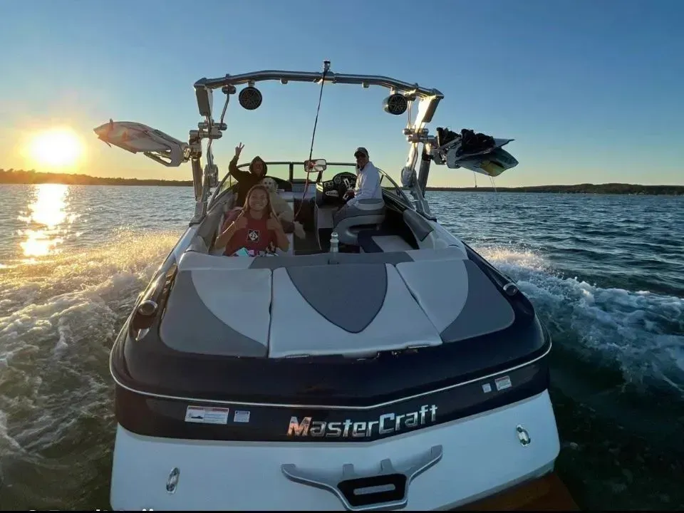 People on a MasterCraft boat speeding across choppy water at sunset