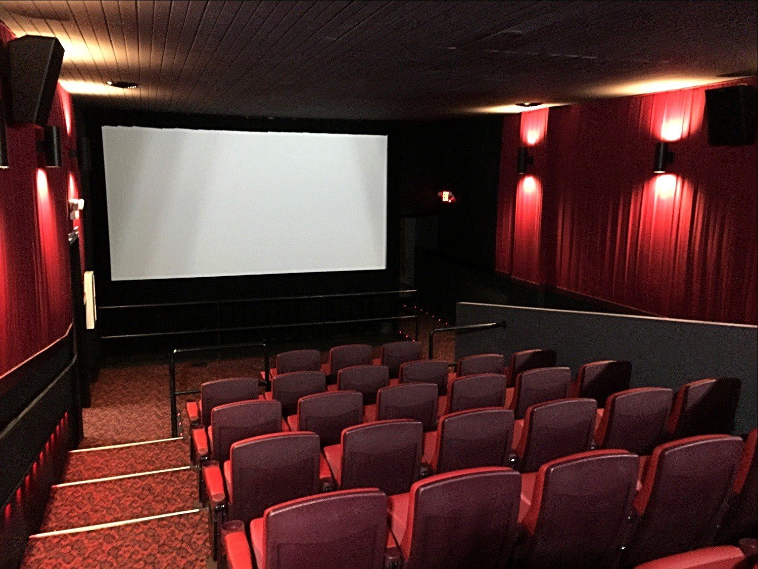 An empty movie theater with red seats and a large screen
