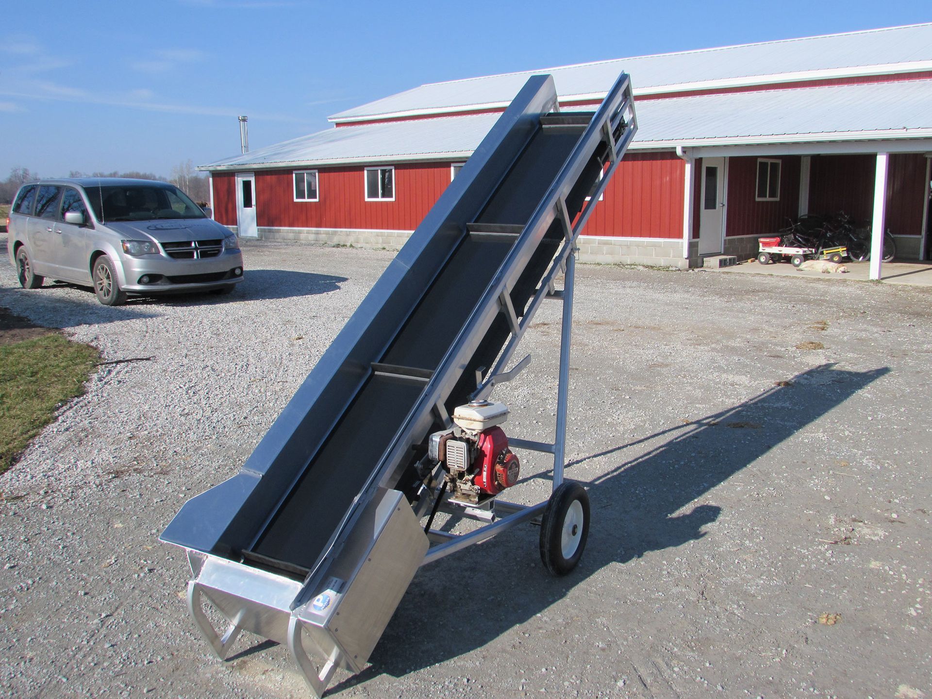 A conveyor belt is parked in front of a red barn